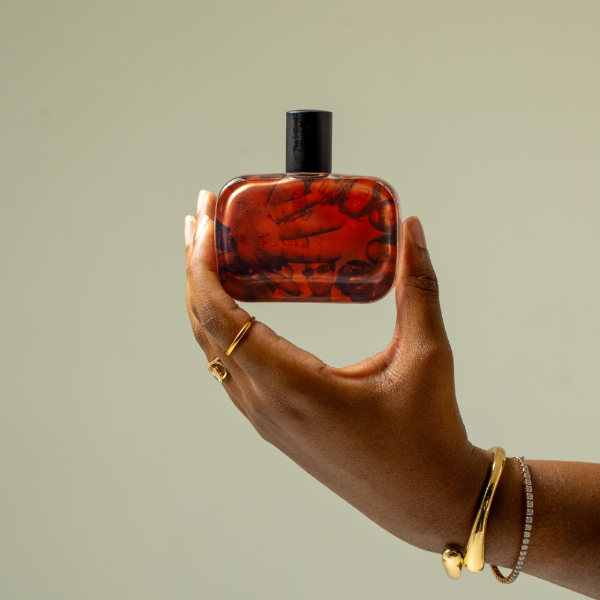 Hand holding the city on a hill perfume bottle against a plain background