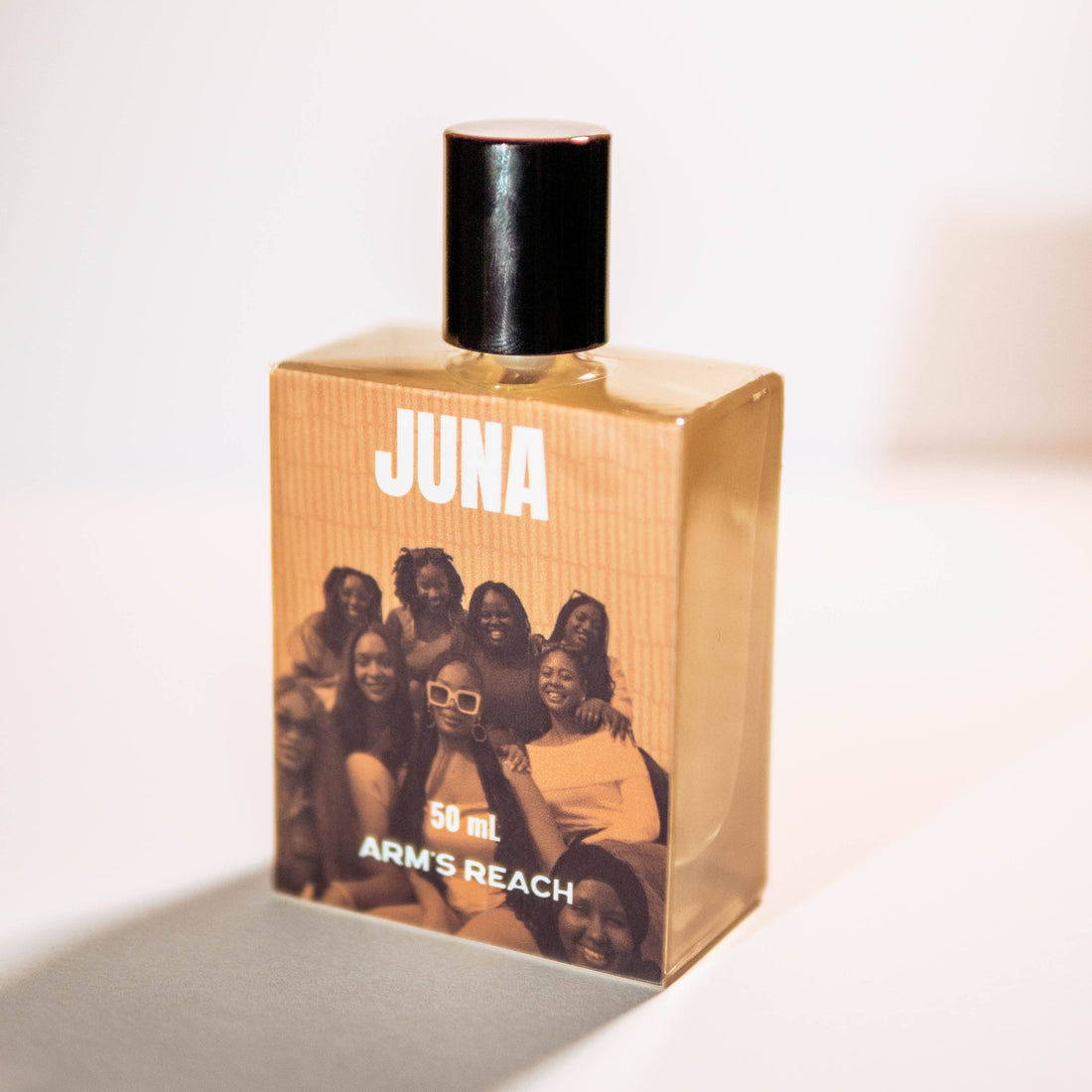 ARM'S REACH JUNA 50 ml perfume bottle with a black cap and a warm wood-grain textured label featuring a group photo of women, set against a plain white background.