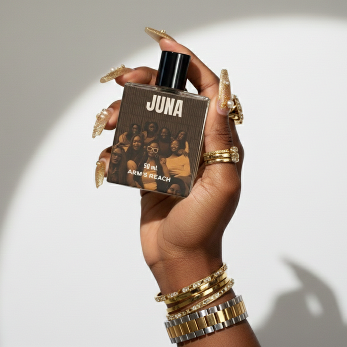 Hand holding a 'JUNA' perfume bottle with a brown label against a white background