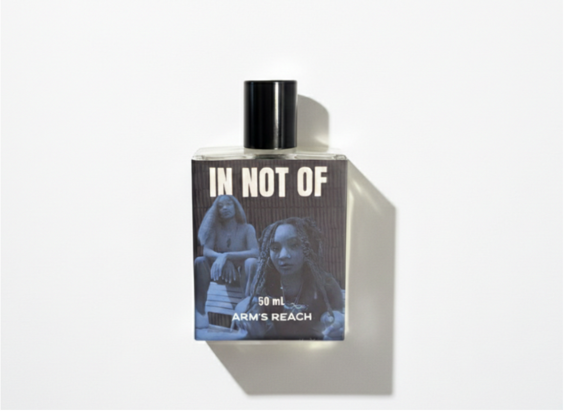 Perfume bottle with 'In Not Of' and 'Arms Reach' text on a white background